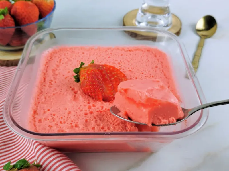 Gelatina de morango com iogurte em um refratário, cortada em quadrados e decorada com morangos