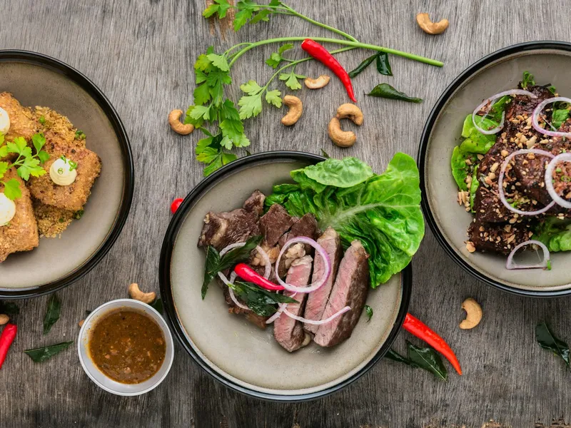Três pratos vistos de cima com carne grelhada fatiada, alface, cebola roxa, pimenta e castanhas de caju