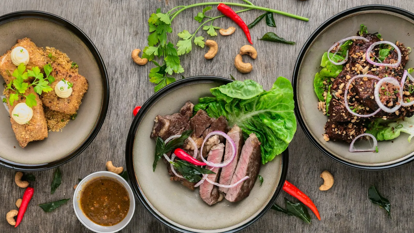Três pratos vistos de cima com carne grelhada fatiada, alface, cebola roxa, pimenta e castanhas de caju