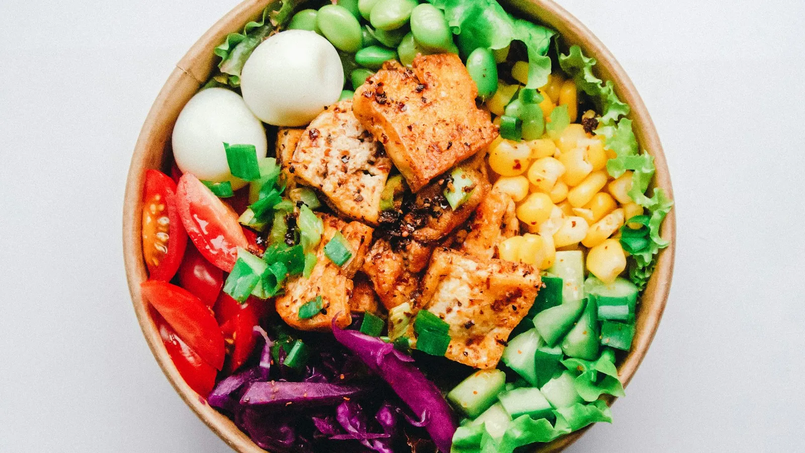 Bowl com tofu dourado, edamame, milho, ovos de codorna, tomate, pepino e repolho roxo